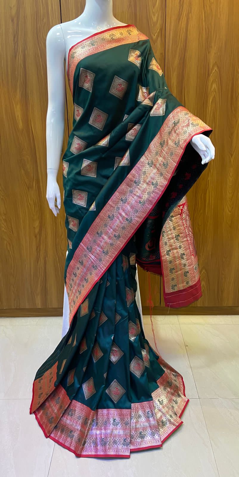 Green saree with red and gold border on a mannequin against a wooden background