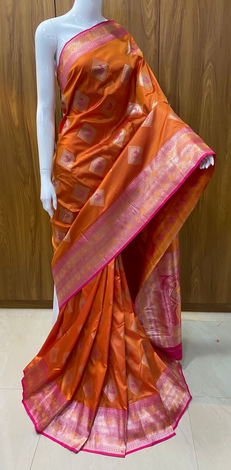 Orange saree with pink border on a mannequin against a wooden background