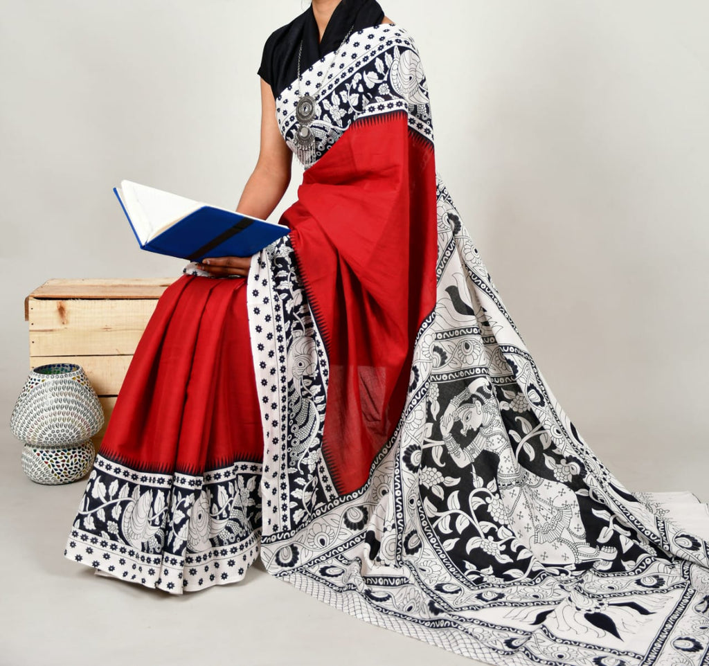 Person wearing a red saree with black and white pattern, holding a book, on a neutral background.