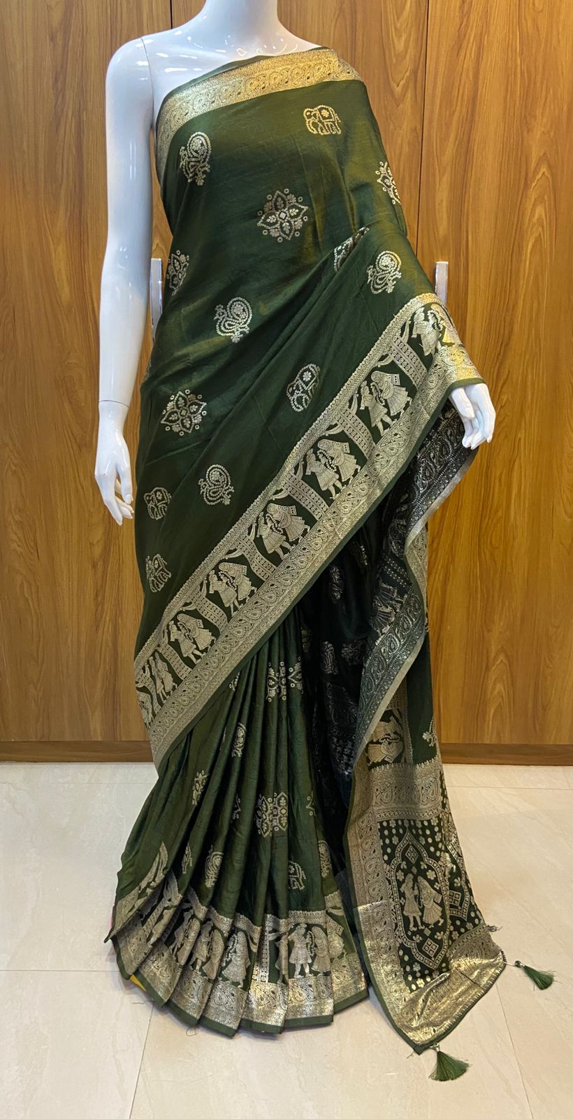 Green saree with gold and white patterns on a mannequin against a wooden background